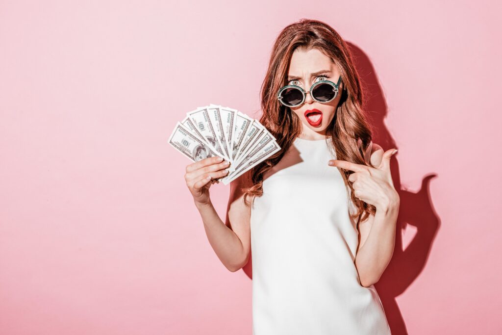 Confused young brunette woman holding money pointing